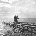 Navy photographer Lt. Charles Kerlee balancing on an outstretched antenna arm aboard the carrier USS Yorktown (Essex-class) while photographing aircraft landings, Oct 1943. Note safety rope around his waist.