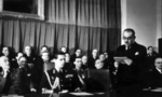 Romanian Premier Nicolae Radescu (left), King Mihai I of Romania (center), Dean of the Medical School Grigore Popa (right edge of photograph), Social Democratic Party leader Constantin Titel Petrescu (behind Mihai I), and others listening to Bucharest University Rector Simion Stoilow at the opening celebration for the 1945-1946 academic year, Bucharest, Romania, circa Dec 1944-Feb 1945