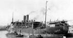 Port quarter view of the passenger-cargo ship SS Tilawa in port with tugs and lighters alongside, 1930s, location unknown.