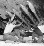 Armorers loading FFAR rockets under the wing of a F4U Corsair fighter, Okinawa, Japan, Jun 1945. Note the sandy mud splatters on the underside of the plane.