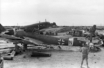 Australian airman inspecting wrecks of Ju 87D (foreground) and Ju 52 (background) aircraft, El Aouina airfield at Tunis, Tunisia, circa May 1943