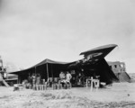 Lieutenant E. T. McBoon, Sergeant C. W. Moore, and Corporal William G. Warrington at a US field kitchen constructed under the wing of a damaged MB.200 bomber, North Africa, 1943
