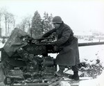 Pvt Paul Romanick of Battery B, 103rd Anti-aircraft Artillery Battalion, US 1st Infantry Division cleaning 40mm anti-aircraft gun, Sourbrodt, Belgium, 31 Dec 1944; note 6 swastika symbols his 6 kills