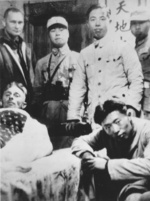 A wounded Doolittle raider lying in a cot, surrounded by John Hilger and Chinese military presonnel, China, Apr 1942