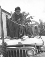 Japanese-American soldier of US 442nd Regimental Combat Team hanging laundry on a jeep in such a way that the vehicle could still be operated in urgent situations, Castellina Sector, Italy, 12 Jul 1944