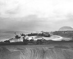 An American bulldozer pulled a road grader on an Iwo Jima beach, 21 Apr 1945, note several Japanese landing ships wrecked on the coast beyond the road