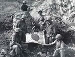 US Marines PFC. J. L. Hudson, Pvt. K. L. Lofter, PFC. Paul V. Parces, Pvt. Fred Sizemore, PFC. Henrey Noviech, and Pvt. Richard N. Pearson posing with a captured Japanese flag, Iwo Jima, Feb 1945
