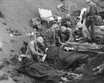 US Navy doctors and corpsmen administer to the wounded at a first aid station, Iwo Jima, Japan, 20 Feb 1945; Chaplain Lieutenant (jg) John H. Galbreath kneeling in right center of photo