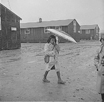 Japanese-American girl walking in rain, Jerome Relocation Center, Denson, Arkansas, United States, 12 Mar 1943