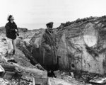 US Navy Lieutenant Commander Knapper and Chief Yeoman Cook of USS Texas examining a damaged German pillbox at Pointe du Hoc, Normandy, France, 6 Jun 1944; note covered dead US Army Ranger at right