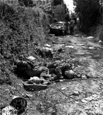 Three dead German soldiers laying on a road near Sainteny, Normandy, France, 16 Jul 1944; note Volkswagen-made Schwimmwagen vehicle and two American soldiers in background