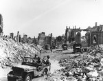 View of the town of Valognes, devastated by Allied bombing during the Cherbourg battle, 24 Jun 1944; note jeep 