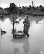 US Marine Staff Sergeant A S. Barnacle shaving in his camp on Okinawa, Japan, ignoring the heavy flooding due to rain, 28 May 1945