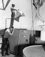 US Navy Signalman 2nd Class Kenneth Mitchell of battleship Colorado sending a message with semaphore flags, 29 Oct 1943; Signalman 3rd Class John Wilson on telescope