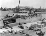 Aircraft transport ship USS Kitty Hawk at Berth F-1, Ford Island, Pearl Harbor, Hawaii, Mar 1942. Note AT-6 Texans and J2F Ducks on top deck with wings removed and trucks on lower deck.