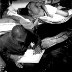African-American US Navy sailors STM1/c Thomas L. Crenshaw (looking at photos) and his bunkmate (writing letter) aboard USS Ticonderoga, off Philippine Islands, 4 Nov 1944