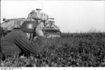 German soldier with binoculars in the Flanders region of France or Belgium, Jun 1944; note PzKpfw 35 S 739(f) medium tank in background