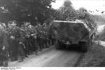 A camouflaged SdKfz. 251 halftrack vehicle passing a column of German troops, France, Jun 1944