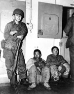 US Marines guarding 2 North Korean prisoners aboard a transport ship which was probably traveling from Hungnam to Busan, Korea, late Dec 1950; note M1 Garand rifle with safety at 