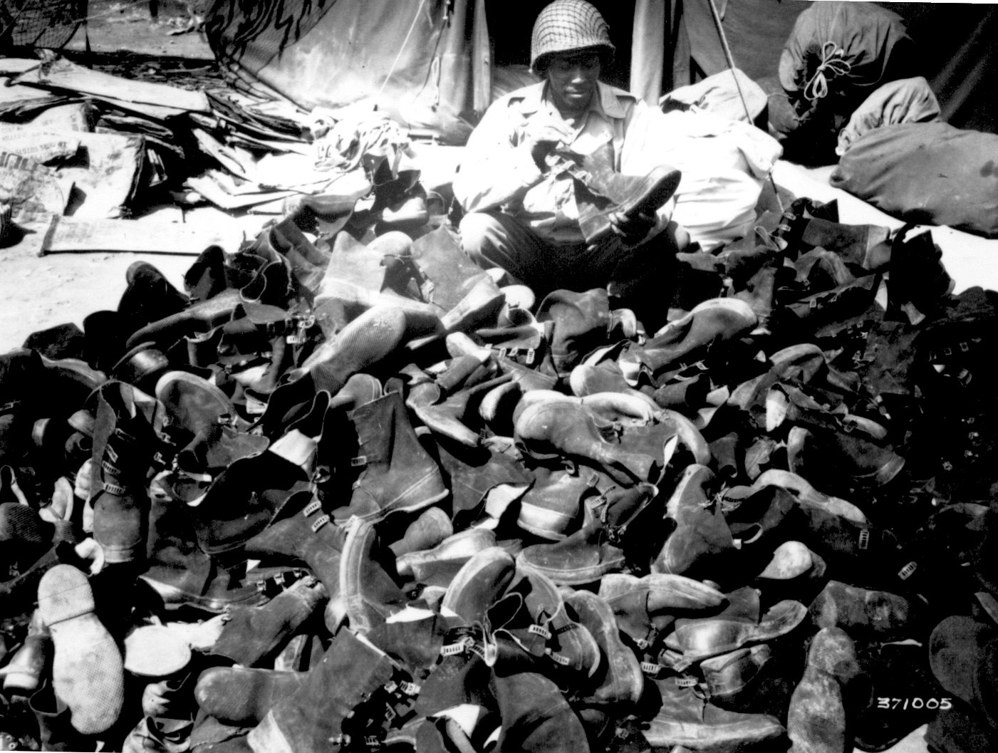 US Army 3278th Quartermaster Company African-American Private Robert Askew examining a pile of overshoes, 8 Apr 1944