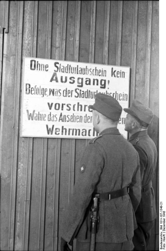 Two German soldiers before a sign noting that to leave the city one would need a permit, Finland or Norway, Dec 1943