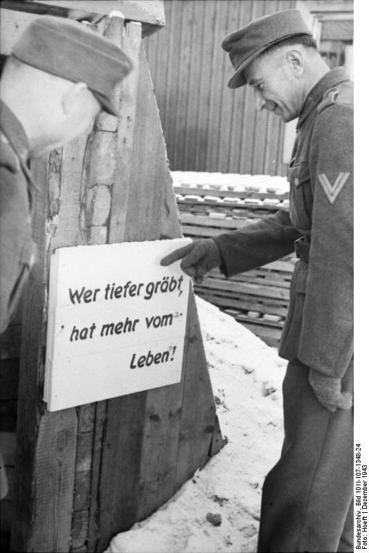 Two German soldiers before a sign noting that 'whoever digs deeper has better chance of survival', Norway or Finland, Dec 1943