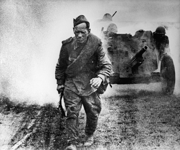 A Soviet soldier walking along a road in Russia, 1 Aug 1943; note field gun in background