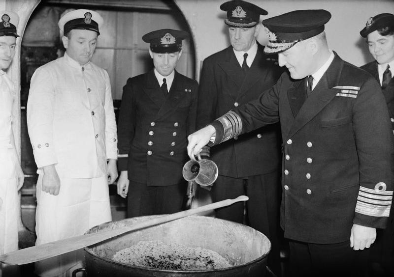 Bruce Fraser pouring rum into the Christmas pudding mix aboard HMS Duke of York, late Nov 1943; note Director of WRNS V. Laughton-Matthews in background