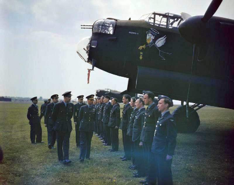 King George VI inspecting ground crewmen during his visit to No. 617 Squadron (Dambusters) and No. 57 Squadron at RAF Scampton, Lincolnshire, England, United Kingdom, 27 May 1943; note Lancaster B Mk I bomber 'Frederick III', the aircraft of Wing Commander Campbell Hopcroft, commanding officer of No. 57 Squadron