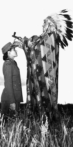 Private Mary Greyeyes (kneeling) and Councilor Harry Ball (dressed as a chief) in a propaganda photograph, Piapot, Saskatchewan, Canada, late Jun 1942