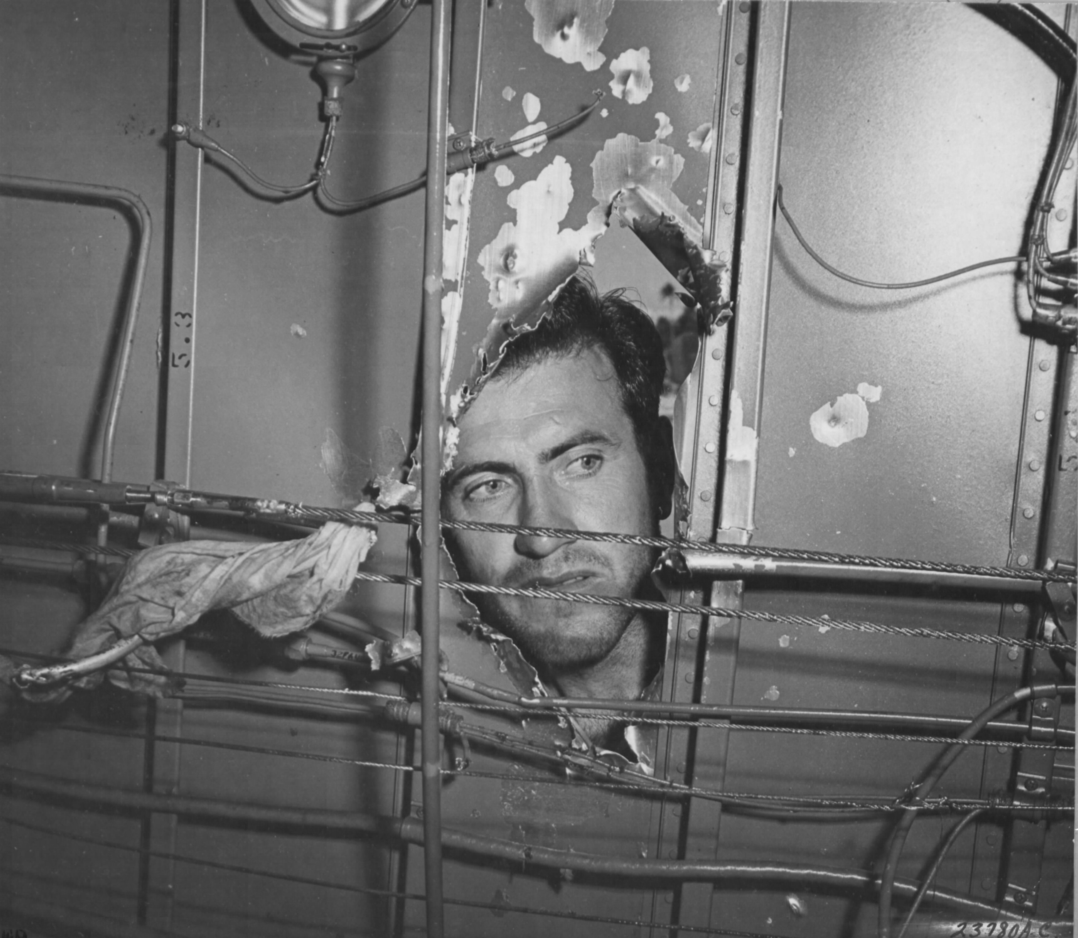 1Lt Louis Zamperini, bombardier of this B-24D Liberator 'Superman' peering through a hole in the aircraft from a 20mm shell over Nauru, Apr 20 1943; photo taken at Funafuti, Gilbert Islands; photo 2 of 3