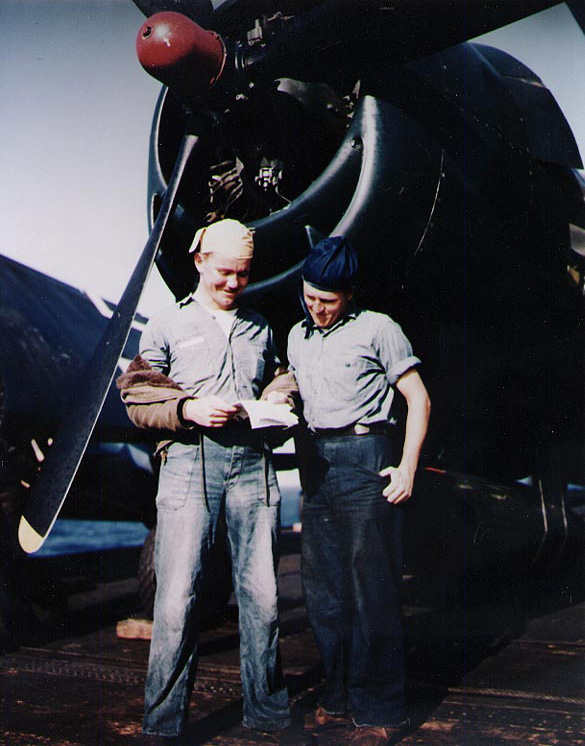 US Navy Seamen 1st Class A. D. Allison and J. W. Roberts reading a letter on Belleau Wood's flight deck next to a F6F Hellcat fighter, circa 1945