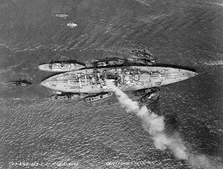 Aerial photo of battleship Colorado in a harbor, 2 May 1927; note three large and five small harbor tugs nearby