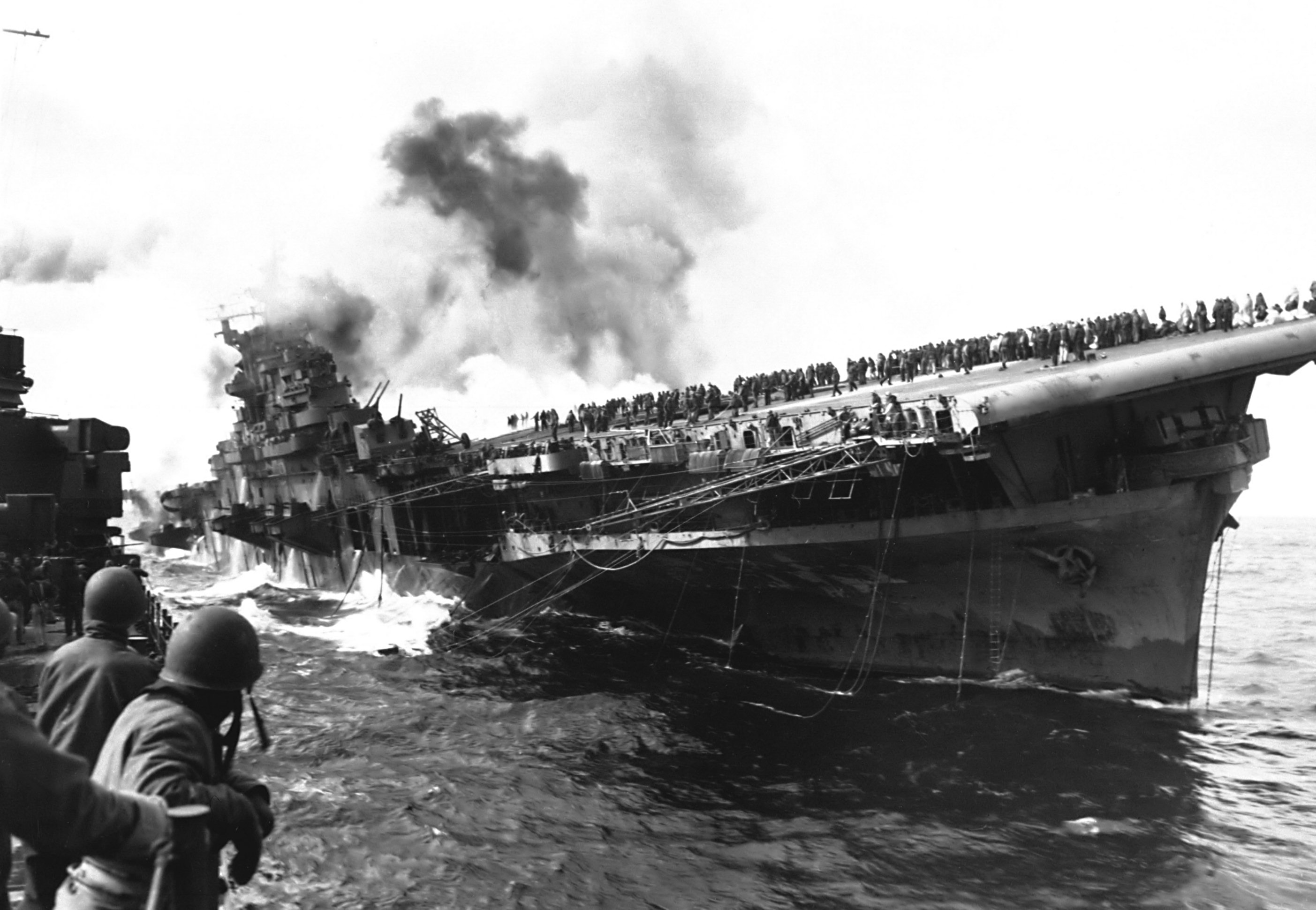 Franklin listing and afire after being hit by two bombs, off Japan, 19 Mar 1945; photograph taken from cruiser Santa Fe