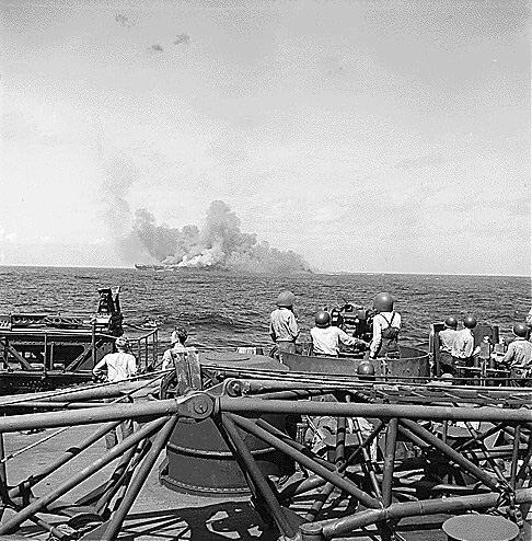 Intrepid smoking after being hit by Japanese special attack aircraft, seen from battleship New Jersey, 25 Nov 1944; note New Jersey's 40mm guns in foreground
