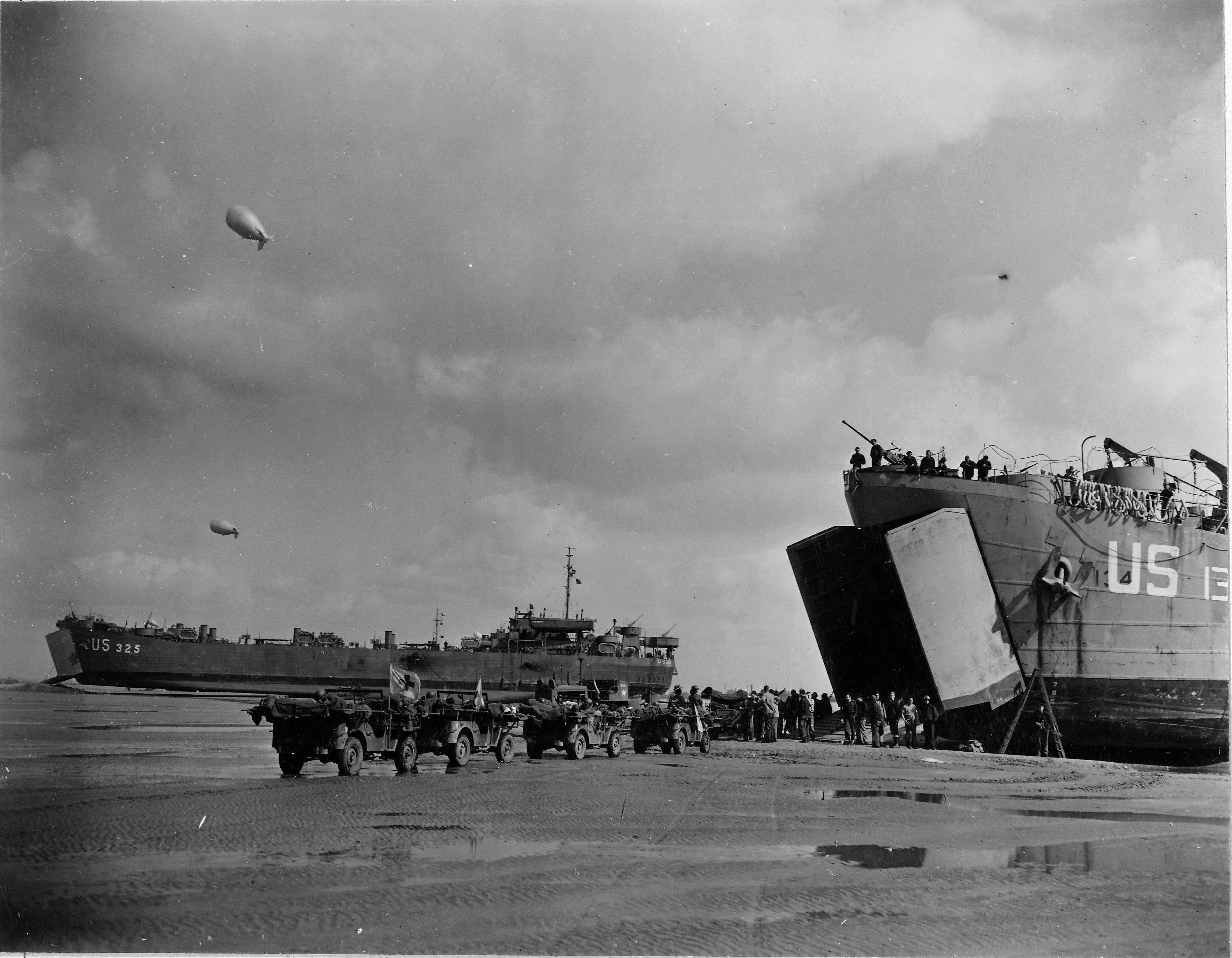 US Navy LST-134 and LST-325 beached at Normandy, France as jeeps driving along the invasion beach carry casualties to the waiting vessels, 12 Jun 1944, photo 1 of 4