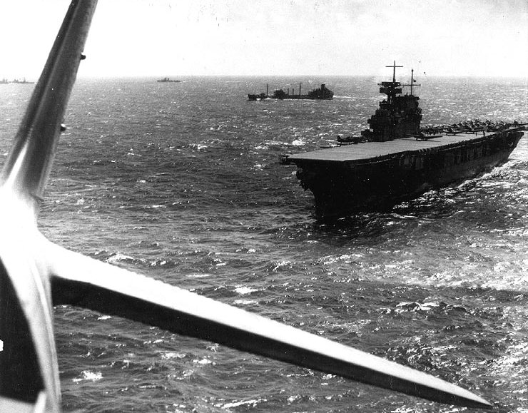 USS Yorktown seen from a TBD-1 aircraft, Pacific Ocean, Apr 1942; note F4F-3 Wildcat fighter preparing for takeoff, and fleet oiler USS Guadaloupe, a destroyer, and a cruiser just beyond