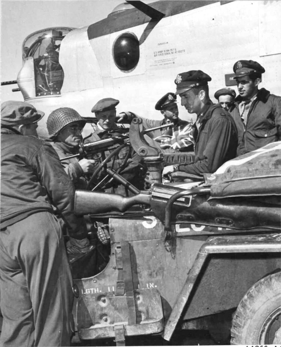 US armored division troops letting an 8th Air Force officer try a German MP 40 machine pistol, England, United Kingdom, 1943-1945; note Jeep vehicle, B-24H bomber, and M1 Garand rifle