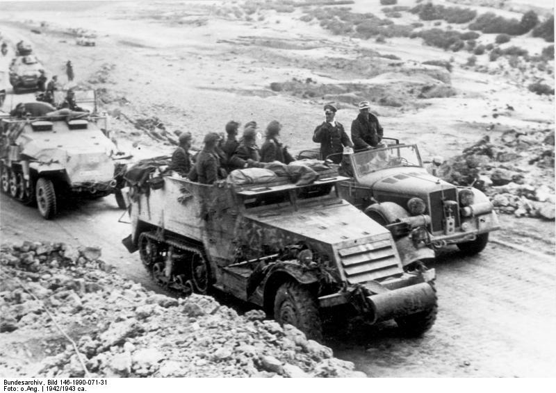 General Erwin Rommel and Lieutenant Colonel Fritz Bayerlein in an open car speaking to motorized troops, North Africa, 1942; note captured US M3 halftrack and German SdKfz. 251 halftrack vehicles