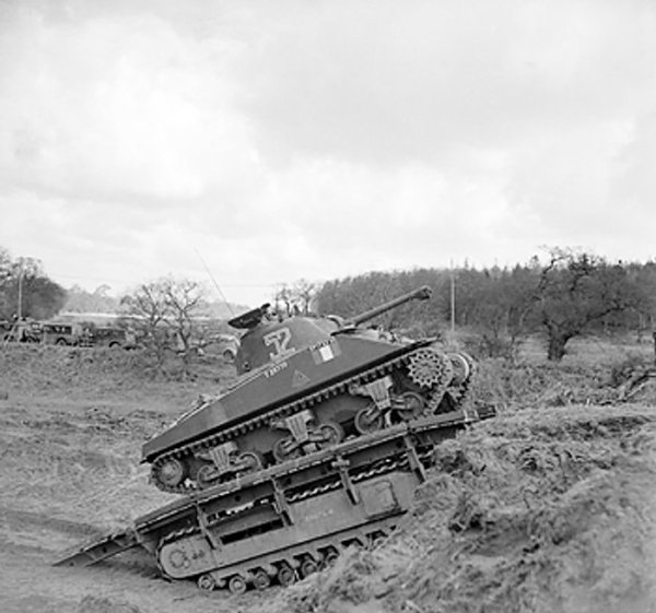 Sherman tank of UK 79th (Experimental) Armored Division Royal Engineers using a Churchill Ark armored ramp carrier to climb a small escarpment, 13 Feb 1944