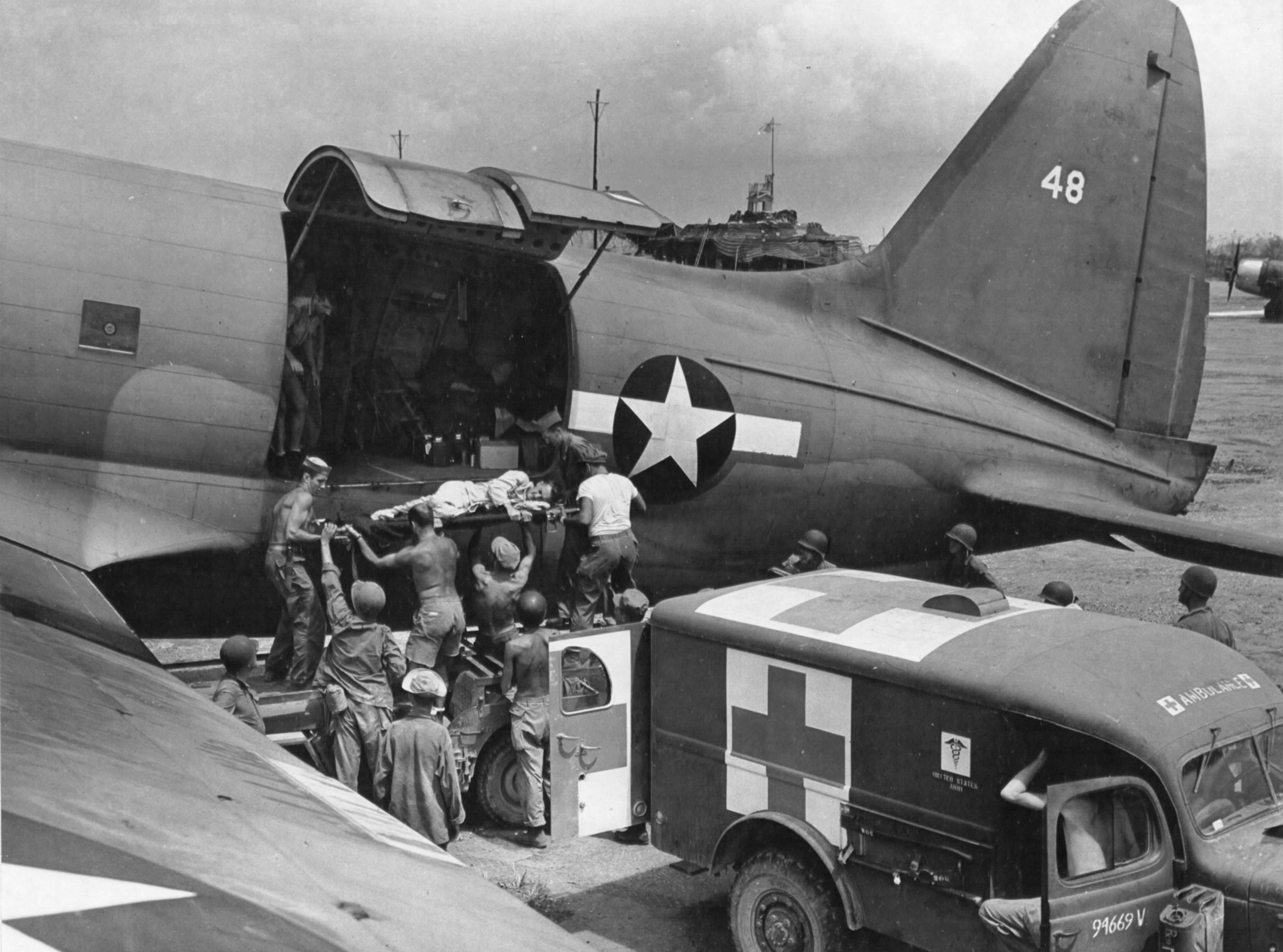 A Marine on Saipan was transferred to an R5C-1 Commando aircraft from a Dodge WC54 3/4-ton field ambulance for transfer to Hawaii, 1944; note the Jeep in between