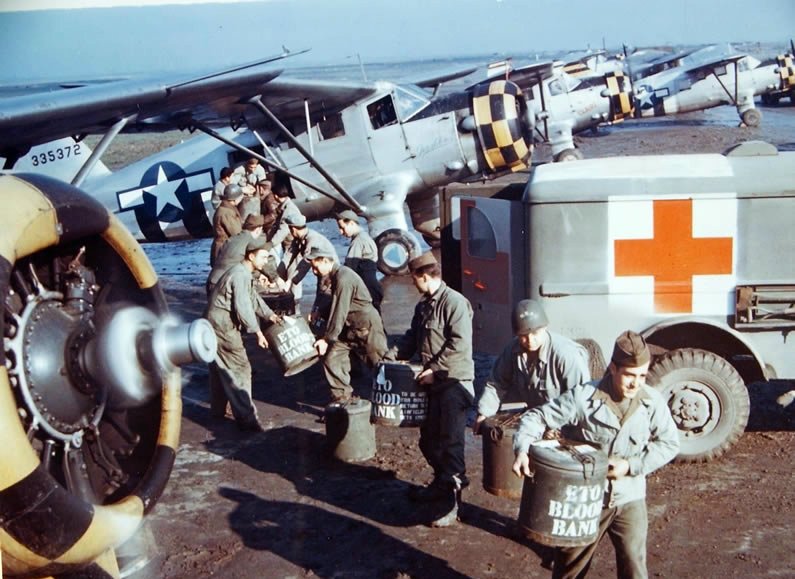 Marmite cans with blood collected from rear echelon troops in England, United Kingdom were being transferred from Dodge WC54 Ambulance to waiting Noorduyn UC-64A Norseman for air transport to Normandy