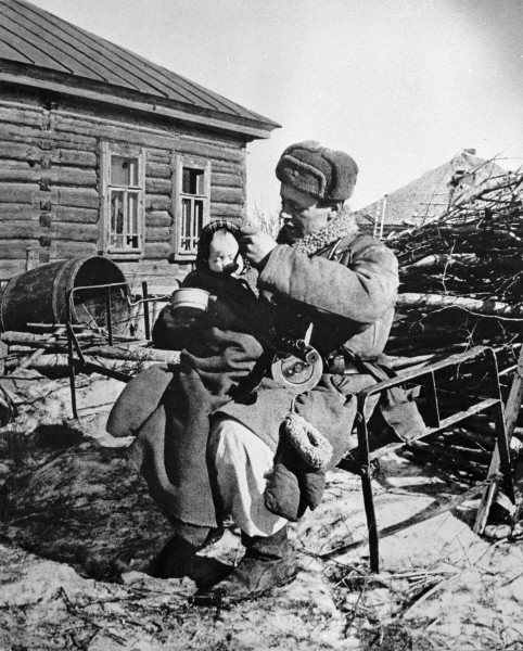 Soviet soldier taking care of a war orphan, Russia, 1943; note PPSh-41 submachine gun in soldier's lap
